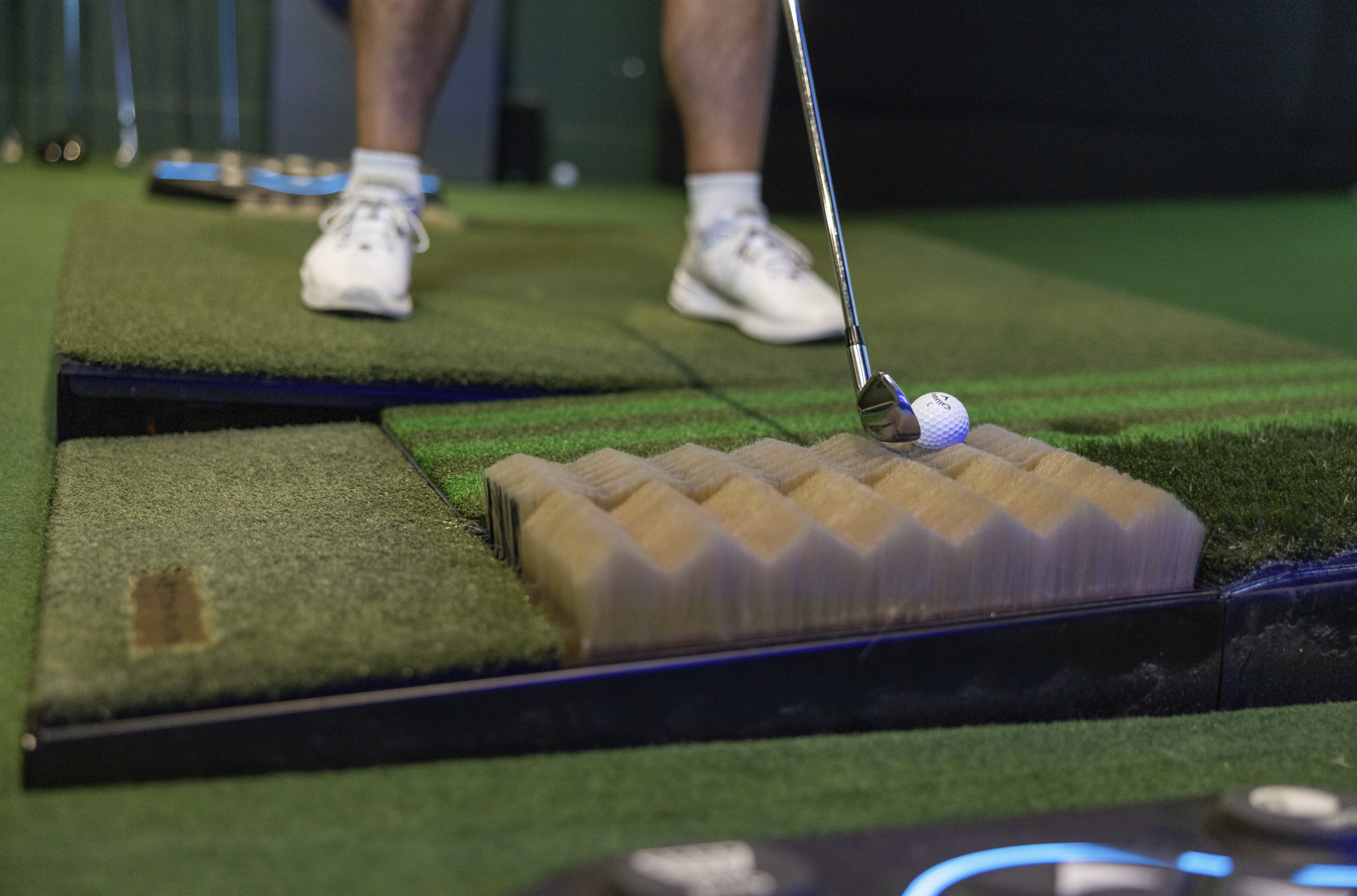 Golfer playing on a GOLFZON TwoVision NX moving floor plate at a Golf Envy indoor golf club