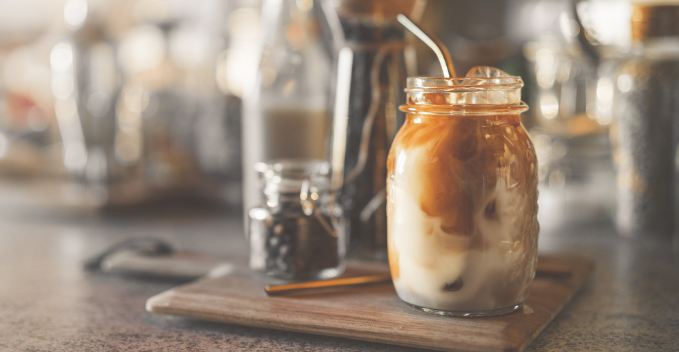 A mason jar filled with iced latte and a metal straw, sitting on a counter